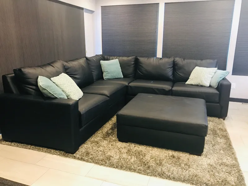 Slide: The Image of Black leather sectional sofa with teal pillows and matching ottoman on a beige rug. - 24