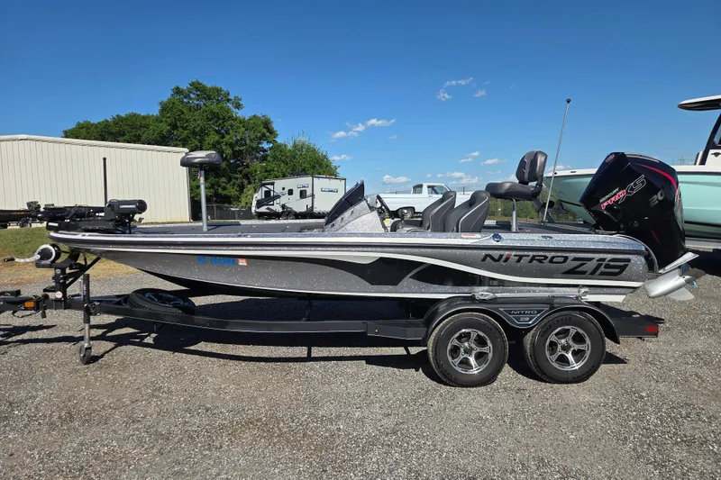 The Image of 2023 Nitro Z19 boat on trailer, parked outdoors under clear blue sky. - 0