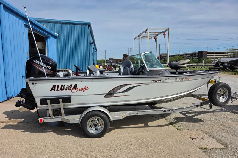 The Image of 2016 Alumacraft Trophy 175 boat on trailer, parked near blue building. - 1