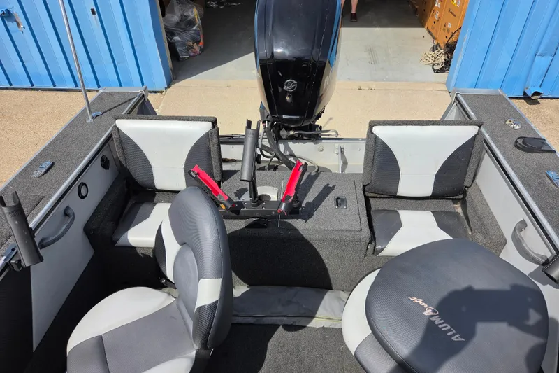 Slide: The Image of 2016 Alumacraft Trophy 175 boat interior with seating and motor, parked near blue building. - 8