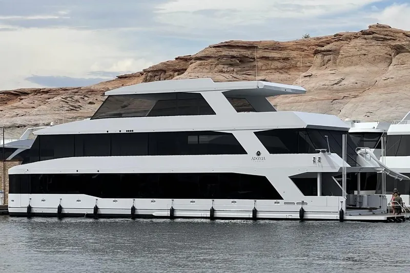 The Image of Luxurious 2021 Adonia houseboat docked by rocky shoreline under cloudy sky. - 0