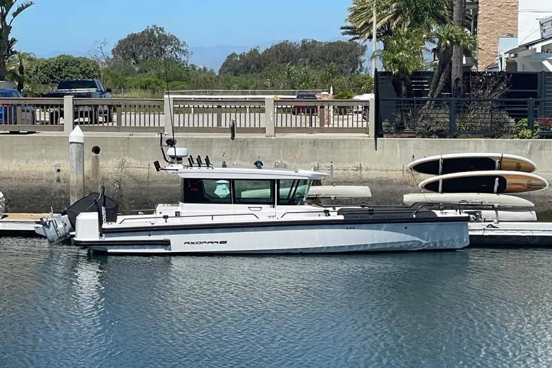 Slide: The Image of 2022 Axopar Brabus 28 Cabin boat docked in a marina, surrounded by calm water. - 3
