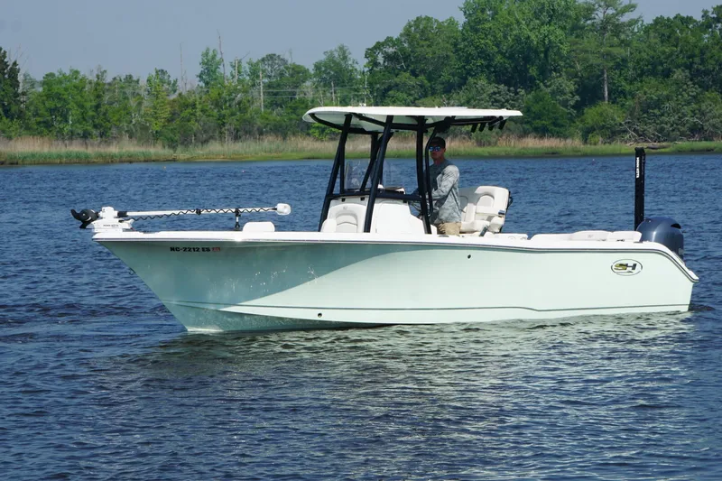 Slide: The Image of 2021 Sea Hunt Ultra 234 boat on a calm lake with lush green shoreline. - 1