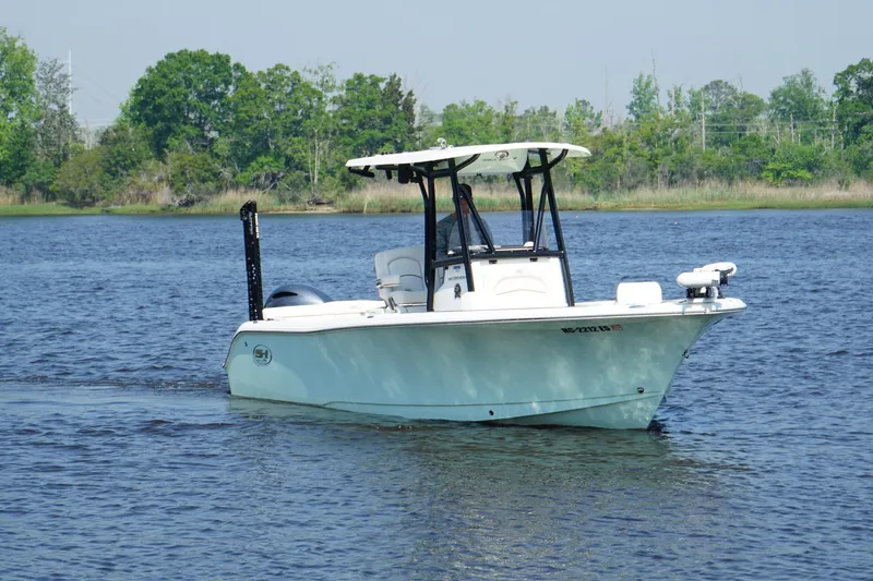 Slide: The Image of 2021 Sea Hunt Ultra 234 boat cruising on a calm lake with lush greenery. - 4