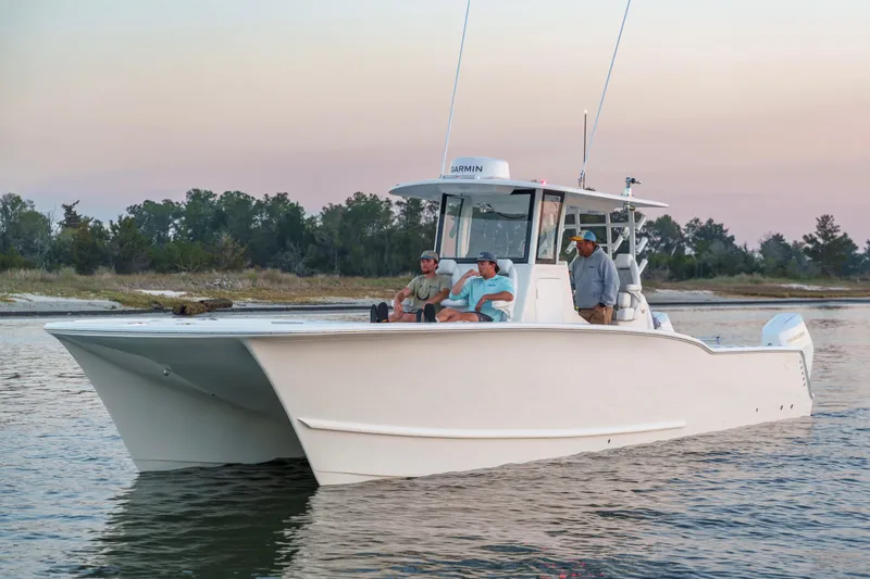 Slide: The Image of 2026 Tideline 365 Offshore boat with three people, cruising near a wooded shoreline at sunset. - 26