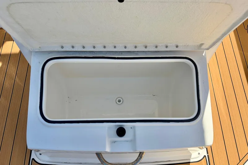 Slide: The Image of Open storage compartment on 2023 Bayliner Trophy T24CC boat, featuring a white interior and wooden deck. - 28