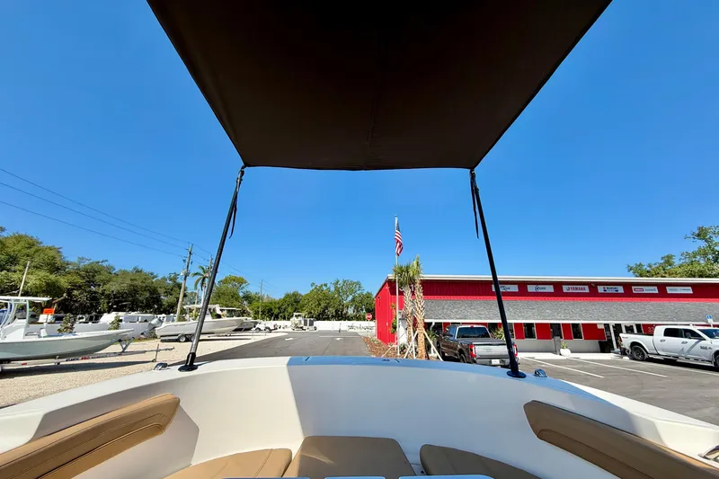 Slide: The Image of 2023 Bayliner Trophy T24CC boat with canopy, parked near a red building under clear blue sky. - 36