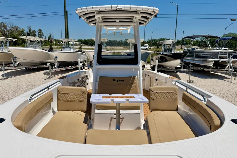 Slide: The Image of 2023 Bayliner Trophy T24CC boat interior with beige seating and table, displayed outdoors. - 8