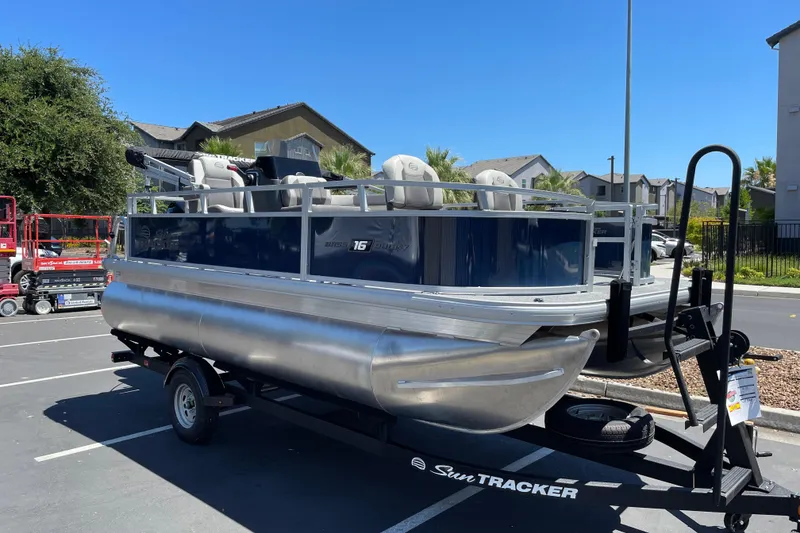 Slide: The Image of 2026 Sun Tracker Bass Buggy 16 XL Select pontoon boat on trailer in parking lot. - 3