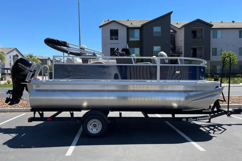 The Image of 2026 Sun Tracker Bass Buggy 16 XL Select pontoon boat on trailer in parking lot. - 0