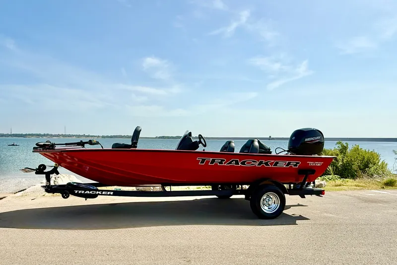 Slide: The Image of Red 2026 Tracker Pro Team 195 boat on trailer by a scenic lake. - 65