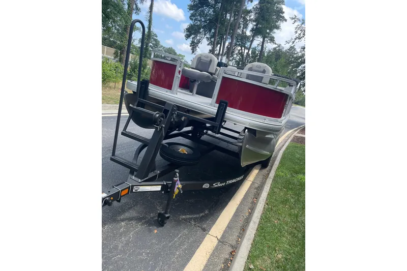 Slide: The Image of 2026 Sun Tracker Bass Buggy 16 XL Select pontoon boat on trailer, parked on roadside. - 6