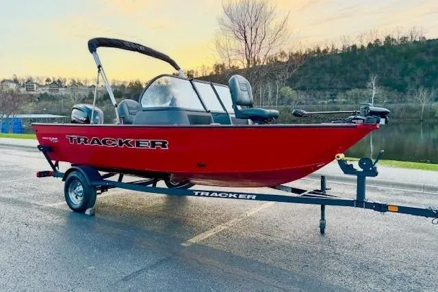 The Image of 2026 Tracker Pro Guide V-16 WT boat on trailer, parked by a scenic lake. - 0