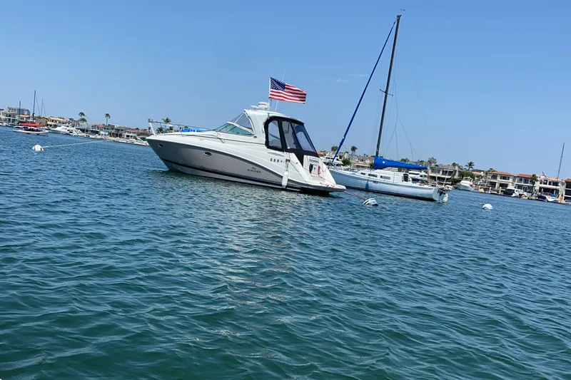 Slide: The Image of 2009 Rinker 340 Express Cruiser anchored in a scenic harbor with sailboats nearby. - 2