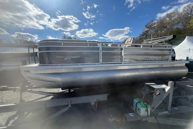 The Image of 2024 Sun Tracker Party Barge 22 DLX pontoon boat on trailer under blue sky. - 0