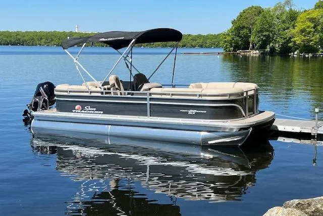 Slide: The Image of 2024 Sun Tracker Party Barge 22 DLX pontoon boat docked on a serene lake. - 2