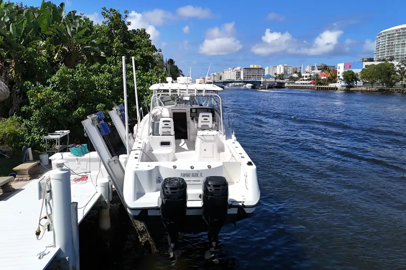 Slide: The Image of 2005 Boston Whaler 305 Conquest docked by a scenic waterfront with lush greenery. - 5
