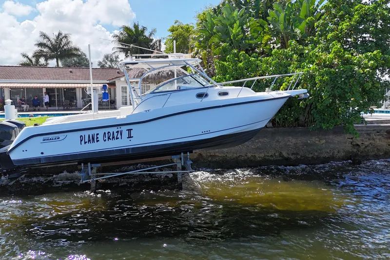 Slide: The Image of 2005 Boston Whaler 305 Conquest boat named "Plane Crazy II" docked by lush greenery. - 6