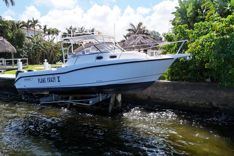 Slide: The Image of 2005 Boston Whaler 305 Conquest boat docked near lush greenery and waterfront homes. - 9