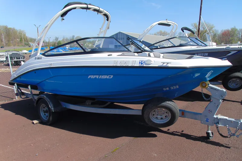 The Image of 2024 Yamaha Boats AR190 on trailer, blue and white design, parked outdoors. - 1