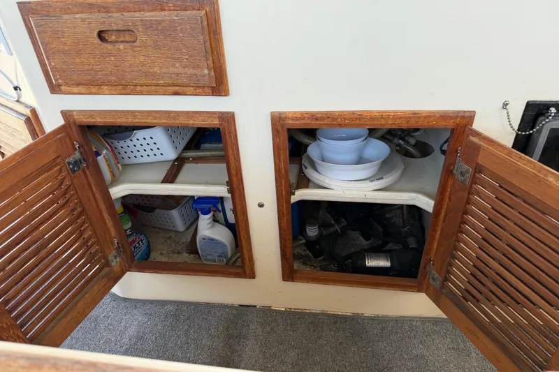 Slide: The Image of Open wooden cabinets on a 1998 Rosborough RF-246 Sedan Cruiser, revealing storage and cleaning supplies. - 37