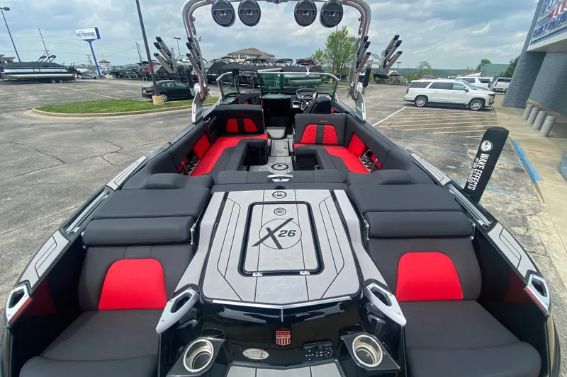 Slide: The Image of 2021 MasterCraft X26 boat interior with red and black seating, parked outdoors. - 10