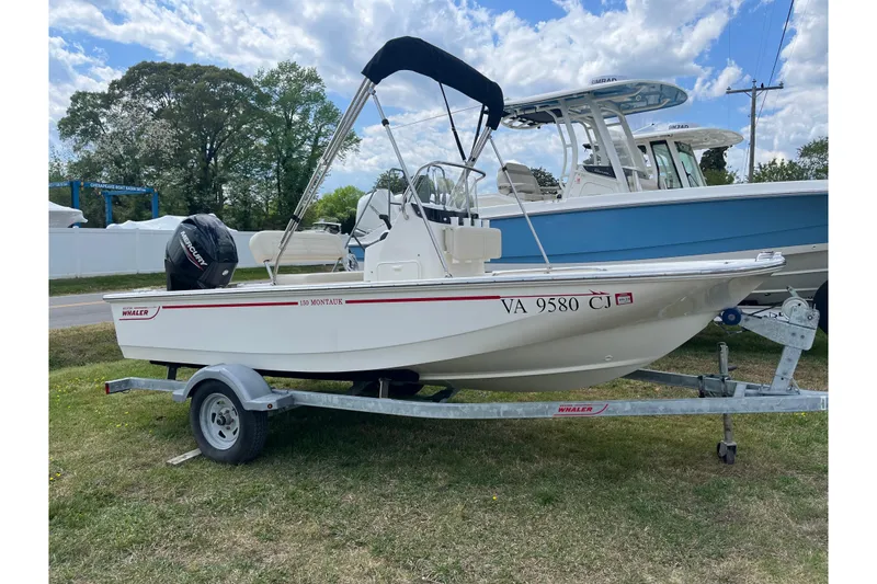 Slide: The Image of 2021 Boston Whaler 150 Montauk boat on trailer, parked on grass under a cloudy sky. - 16