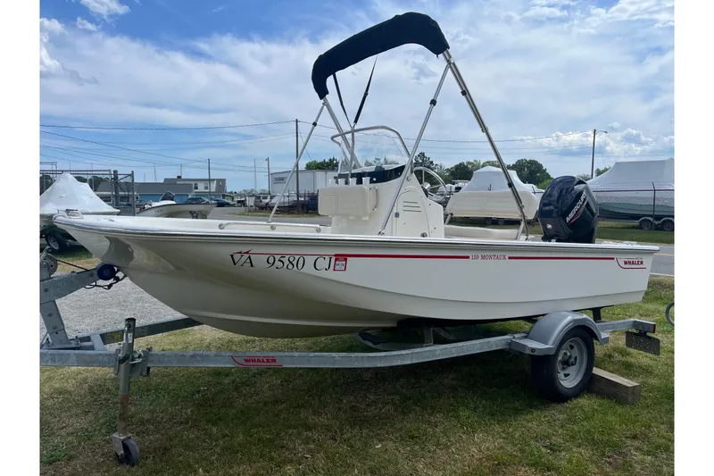 Slide: The Image of 2021 Boston Whaler 150 Montauk boat on trailer, parked outdoors under a blue sky. - 18