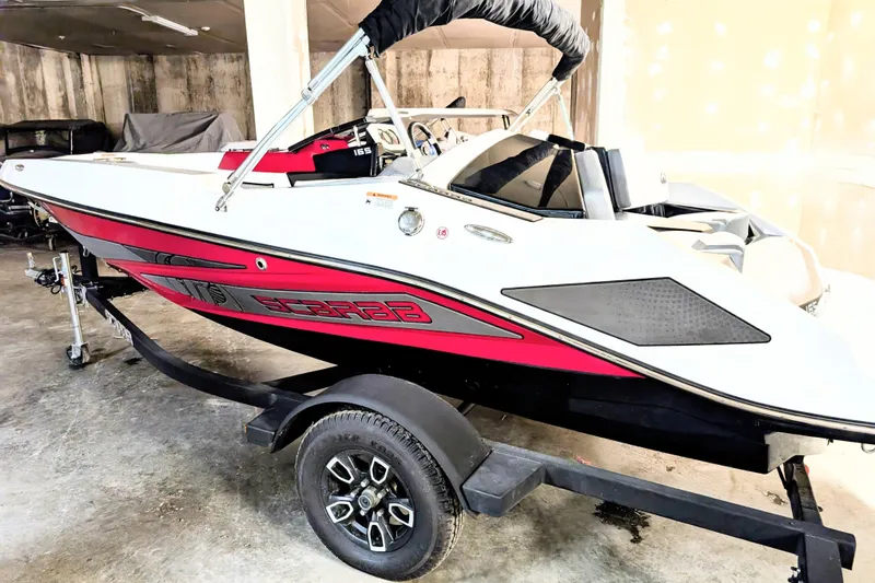 Slide: The Image of 2023 Scarab 165 ID boat on trailer in garage, featuring sleek red and white design. - 2