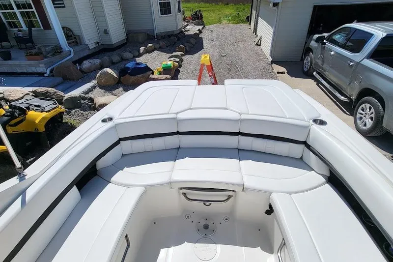 Slide: The Image of 2016 Sea Ray SLX 250 boat interior with white seating, parked near a house and vehicles. - 6