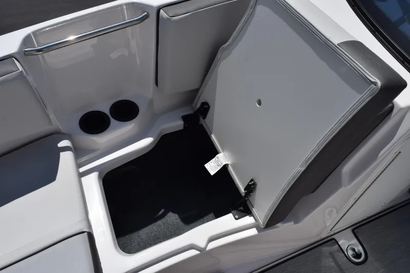 Slide: The Image of 2026 Yamaha Boats AR220 storage compartment with open hatch and cup holders. - 14