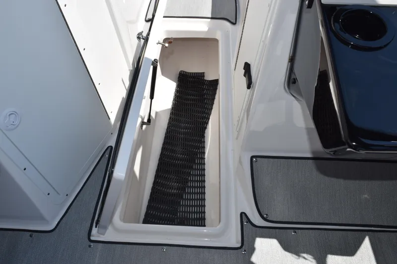 Slide: The Image of 2026 Yamaha Boats AR220 storage compartment with black mat and cup holder. - 18