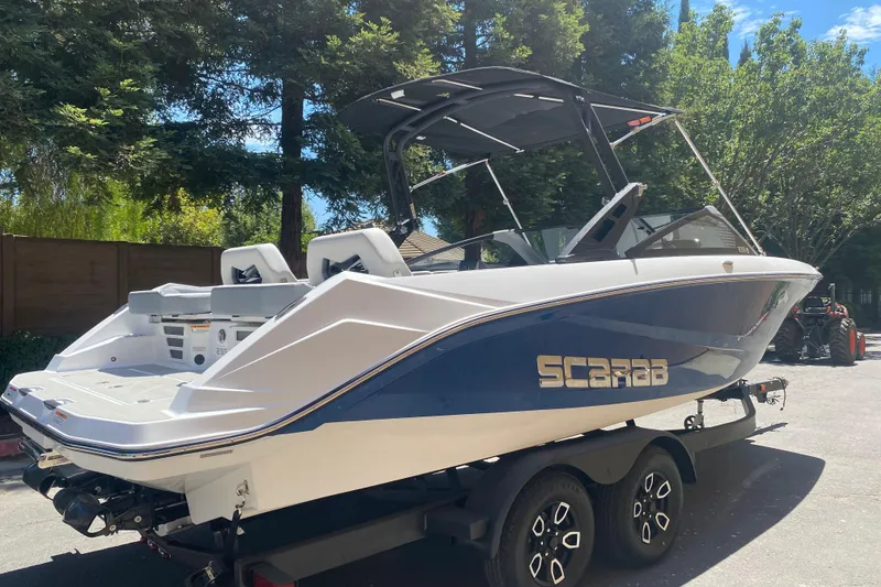 Slide: The Image of 2025 Scarab 235 SE boat on trailer, parked outdoors under trees. - 24