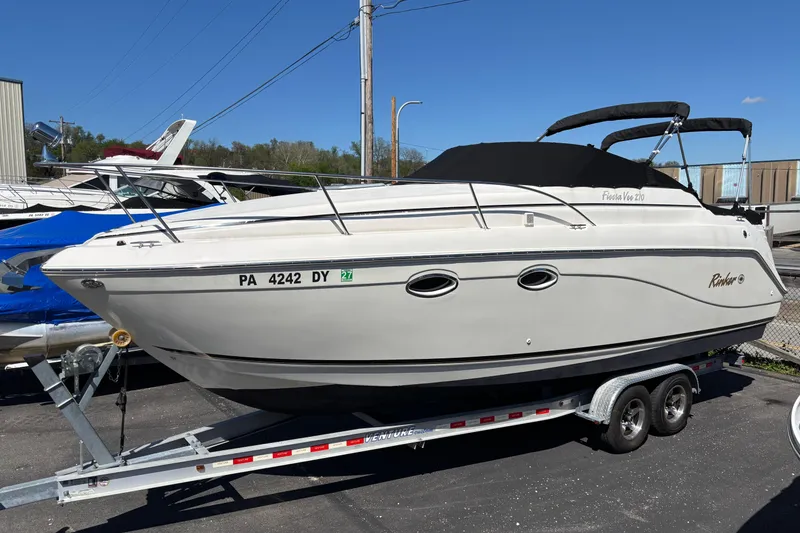 The Image of 2002 Rinker Fiesta Vee 270 boat on trailer, parked outdoors under clear sky. - 0