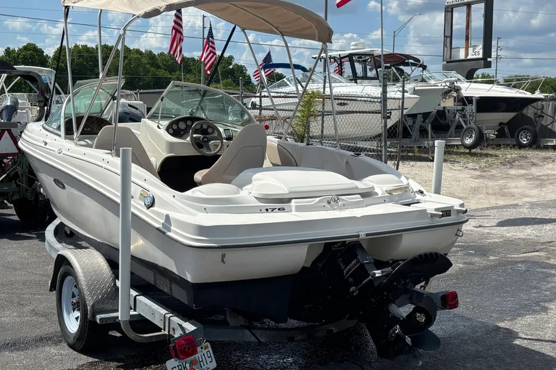 Slide: The Image of 2002 Sea Ray 176 Bow Rider boat on trailer, parked outdoors with flags in background. - 2