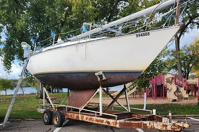 Slide: The Image of 1977 C&C 29 sailboat on trailer, parked near trees and playground. - 15