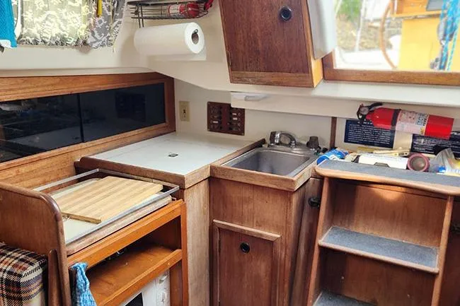 Slide: The Image of 1977 C&C 29 sailboat galley with wooden cabinetry, sink, and storage shelves. - 6