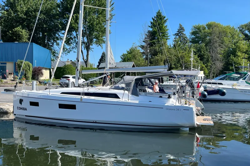 The Image of 2023 Beneteau Oceanis 34.1 sailboat docked in a marina, surrounded by trees and buildings. - 0