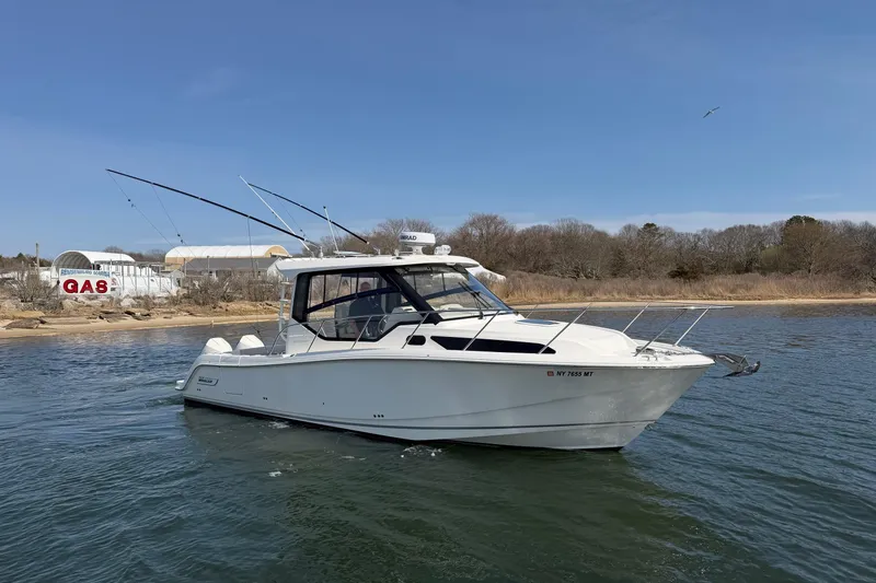 Slide: The Image of 2023 Boston Whaler 325 Conquest boat on water near shoreline with gas station in background. - 44