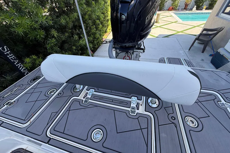 Slide: The Image of 2023 ShearWater x22 boat deck with cushioned seat and outboard motor, near a poolside. - 21