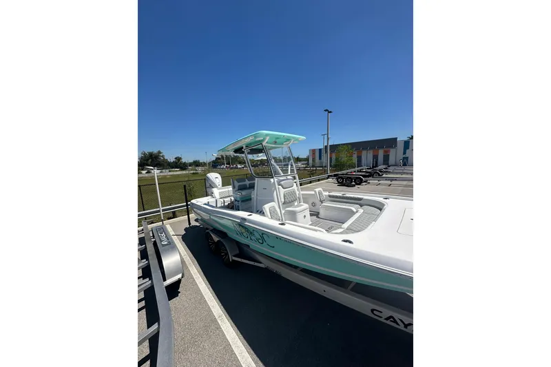 Slide: The Image of 2021 Caymas 28 HB boat with teal accents, parked on a trailer under clear blue sky. - 5
