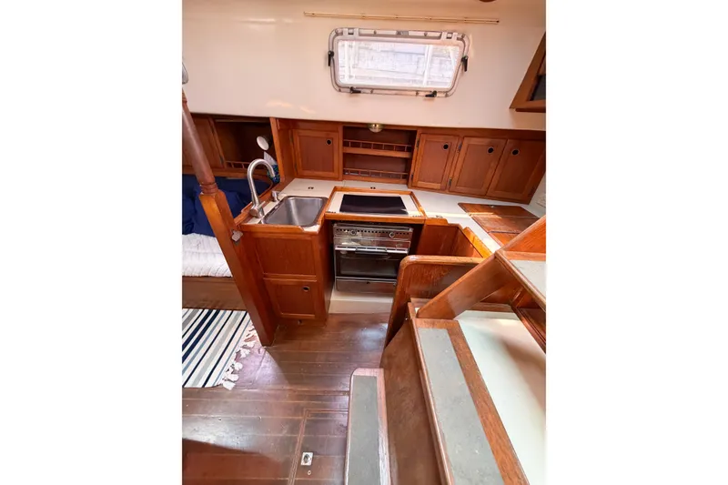Slide: The Image of Interior of 1987 Bayfield 36 sailboat, featuring a compact wooden kitchen with stove and sink. - 31