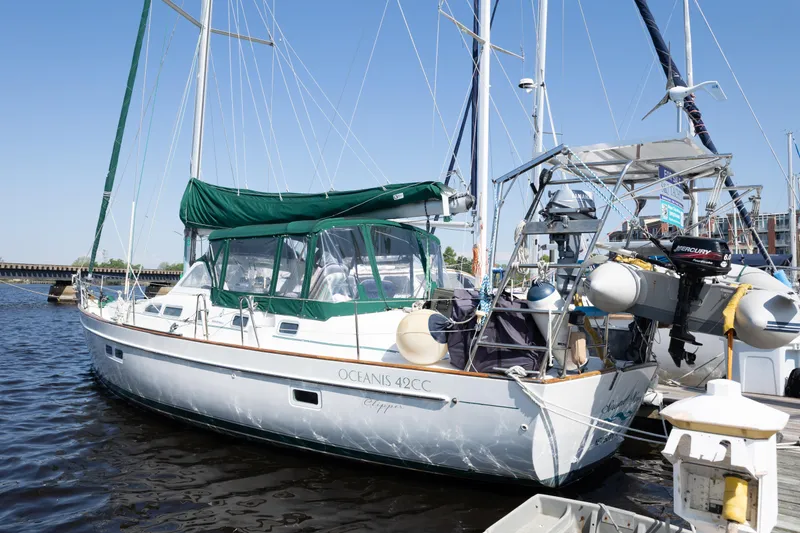 Slide: The Image of 2002 Beneteau Oceanis 42CC sailboat docked in marina, featuring green canopy and outboard motor. - 2
