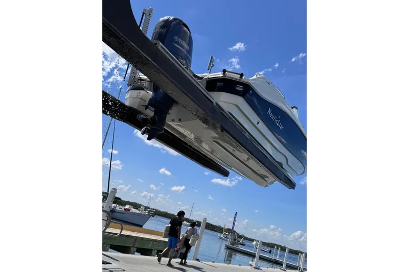 Slide: The Image of 2022 NauticStar 223DC Sport Deck boat with black canopy, docked on gravel. - 12