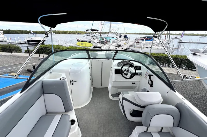 Slide: The Image of 2022 NauticStar 223DC Sport Deck boat interior with seating and steering wheel, docked at marina. - 26