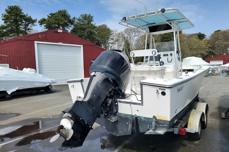 Slide: The Image of 2003 SeaCraft SC 23 Classic boat with outboard motor on trailer, parked near red building. - 13