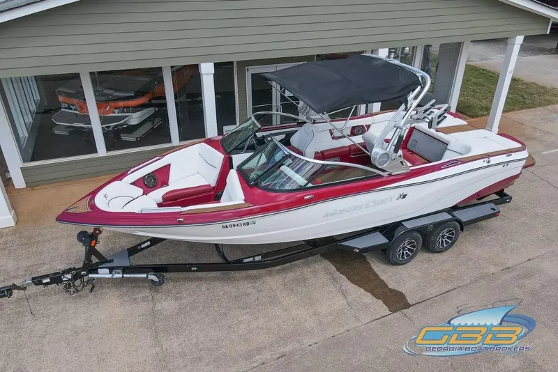 Slide: The Image of 2018 MasterCraft XT25 boat on trailer, red and white design, parked outside a building. - 24