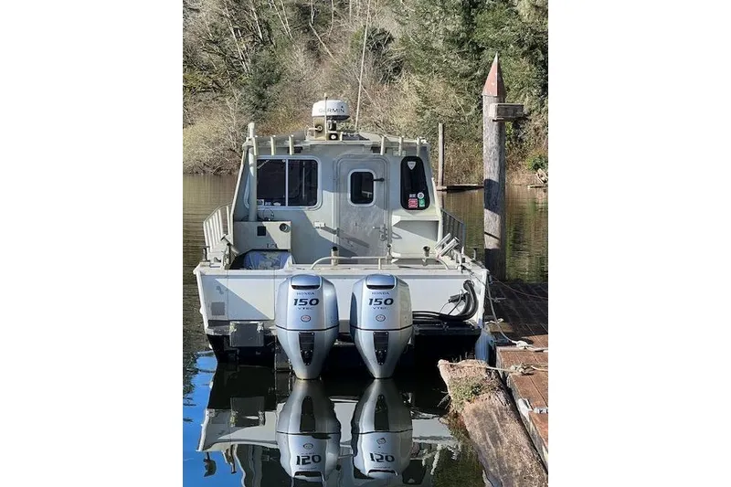 Slide: The Image of 1998 Maxweld Cuddy Hardtop boat with dual Honda 150 engines docked by a forested shoreline. - 29