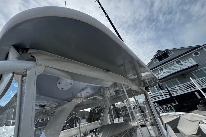 Slide: The Image of 2015 Belzona 32 CC boat with canopy, docked near a waterfront house under a cloudy sky. - 37