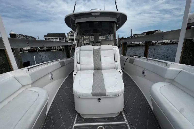 Slide: The Image of 2015 Belzona 32 CC boat interior with white seating and gray flooring, docked by waterfront homes. - 75